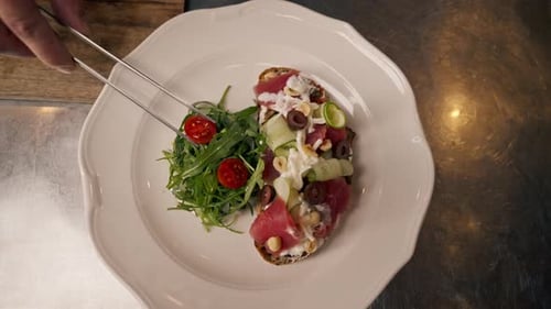 Close-up of chef preparing beef bruschetta with avocado tongs tomatoes in professional kitchen