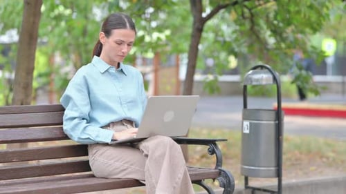 Woman Using Laptop on Bench in Park