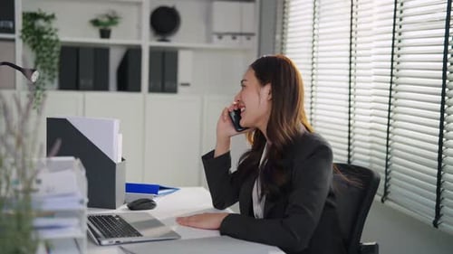 Asian happy businesswoman talking on smartphone while working in office.
