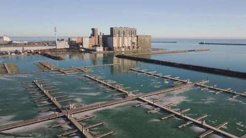 Marina de Port Colborne con muelles vacíos y edificios industriales, día tranquilo, vista aérea