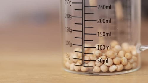Chickpeas pouring into glass storage jar in the kitchen close up, copy space.