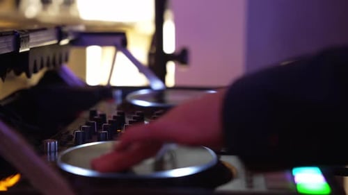 Nahaufnahme eines Hochzeits-DJ, der während einer Empfangsparty mit bunten Lichtern Musik auf einem Plattenspieler mischt