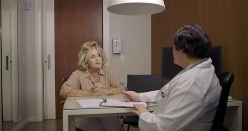 Elderly woman explaining symptoms to female doctor during consultation at medical clinic, seated at