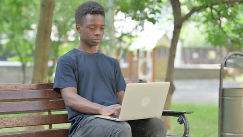 Hombre afroamericano apuntando directamente al espectador con una computadora portátil al aire libre