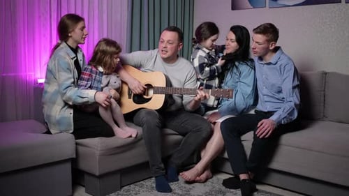 Family Gathers Around Guitar Singing Together at Home