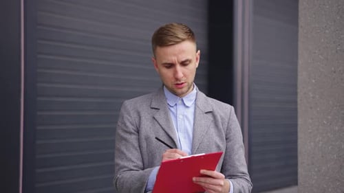 Young Businessman Making Notes in the Documents Outdoors Slow Motion
