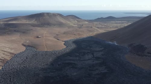 Black basalt rock slow moving lava stream stretching towards ocean, Iceland