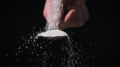 Sugar Pours Into a Spoon on Black Background Slow Motion CloseUp Copy Space