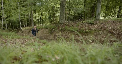 Seitliche Panoramaaufnahme eines Wanderers, der auf einem von grünen Bäumen umgebenen Waldweg den Hügel hinaufgeht