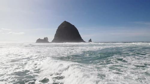 Water rushes past as the shadow of Haystack Rock approaches in the distance