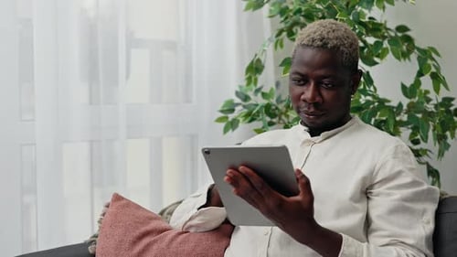 Young Adult Using Tablet on Couch Indoors