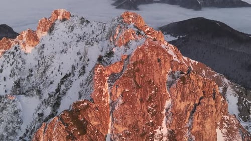 Aerial View of Snowy Rocky Peak Illuminated By Sunset Light with Fog Draping the Valley Below