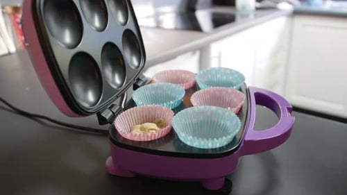 adding cake mixture to paper baking tray with a spoon in a cupcake maker
