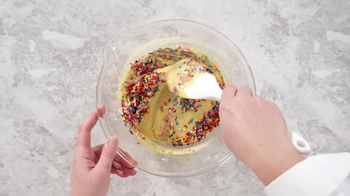 Flach zusammenklappbare Regenbogenstreusel zu einem Kuchenteig in einer Glasrührschüssel legen, um Funfettti Bundt zu backen