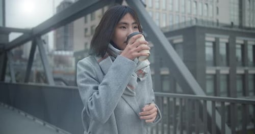 Asian Girl Walks Along a Bridge Crossing Against the Backdrop of a City Landscape