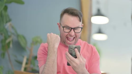 Man Cheering While Looking At Smart Phone Indoors