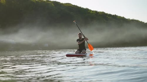 Sportsman Kneeling on Sup Board Paddling on Misty Lake