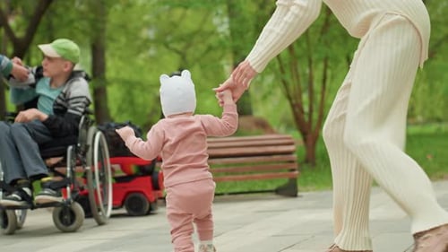Woman Holding Hand of Walking Infant in Park