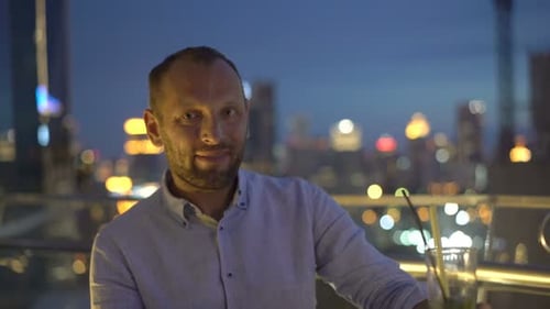 Portrait of Happy, Young Man Sitting on Terrace in Bar at Night 30s