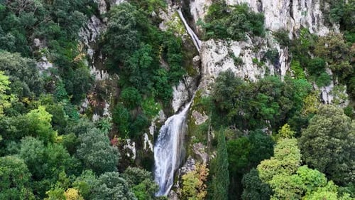 Aerial view of a high waterfall cascading down a steep white rocky cliff face surrounded by dense