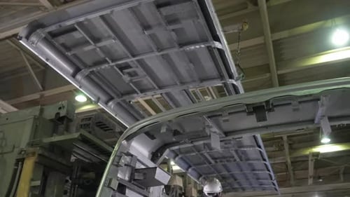 Une grande section de toit métallique est abaissée par une grue sur la carrosserie d'un bus dans une usine d'assemblage