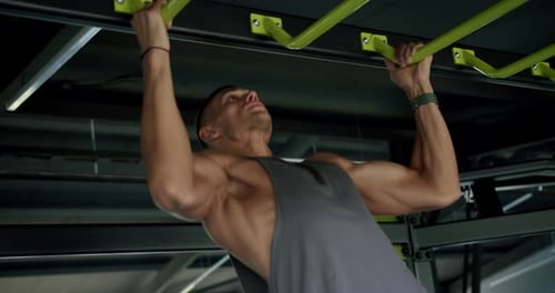 Konzentrierter Mann führt herausfordernde Klimmzüge im modernen Fitnessstudio durch