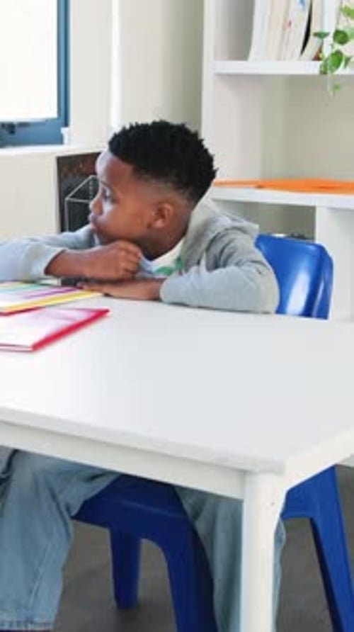 Vertical video: Reading striped notebook at desk, kid in hoodie turning pages then resting, gazing