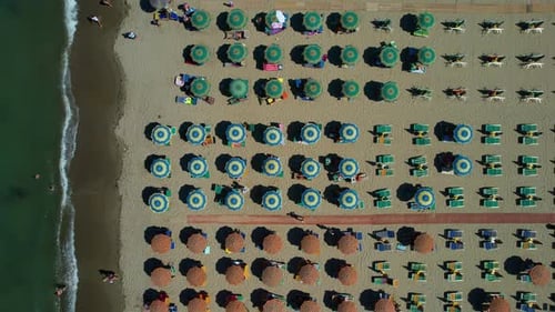 Aerial view of colorful beach umbrellas and sunbeds lined up on sandy beach for summer vacations, Ad