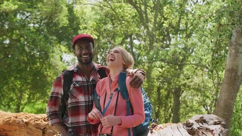 Happy diverse couple with backpacks embracing in park, slow motion