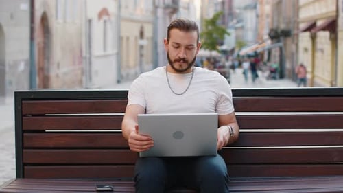 Young Man Freelancer Starts Working on Laptop Sends Messages Makes Online Purchases on City Bench