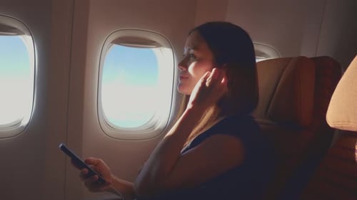 Asian woman using headphone listen to music while sitting in airplane.