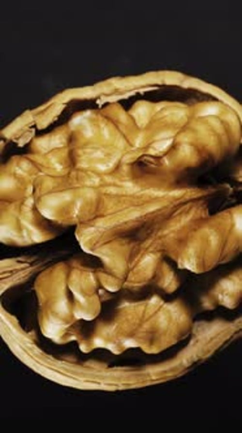 broken in half walnut on a black background rotates. Close-up. View from above. Vertical video.