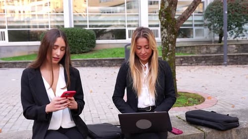 Two Women Work Outdoors on Phones and Laptop