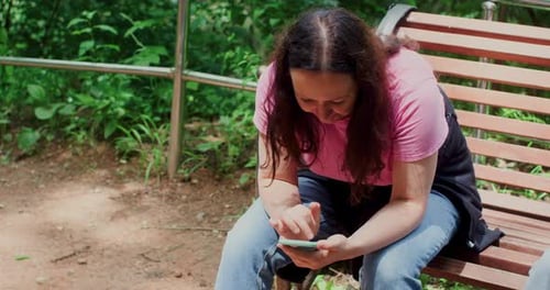 Mature Woman Tourist Texting Message on Smartphone Sitting on Bench in Park