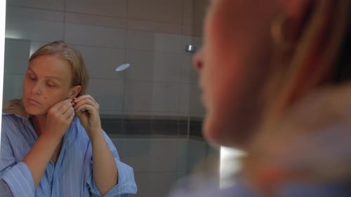 Woman Puts on Earrings in Bathroom Mirror