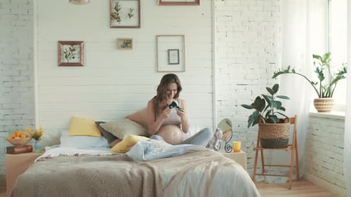Pregnant Woman on Bed Holding Baby Shoes