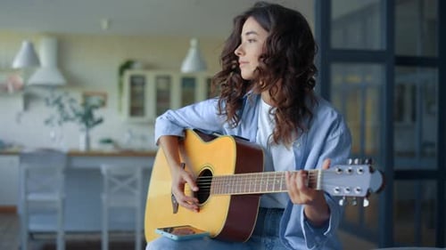 Woman playing acoustic guitar indoors near kitchen
