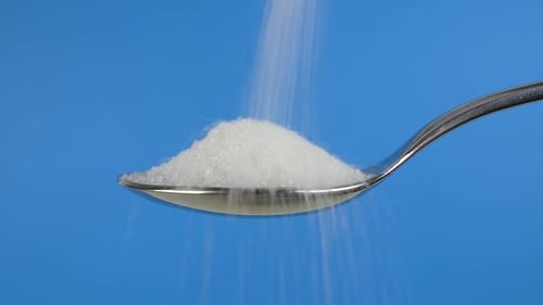 Sugar granules falling into a metal spoon