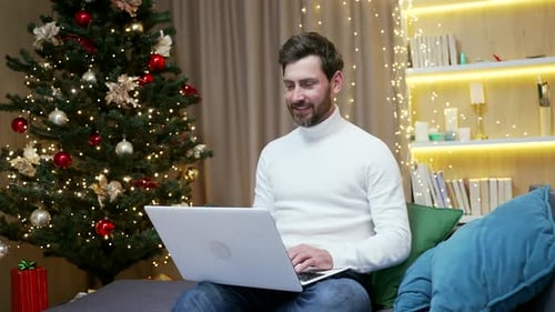 Man Uses Laptop Near Christmas Tree Indoors