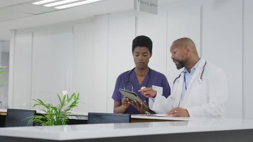 African american male and female doctors using tablet, talking at hospital