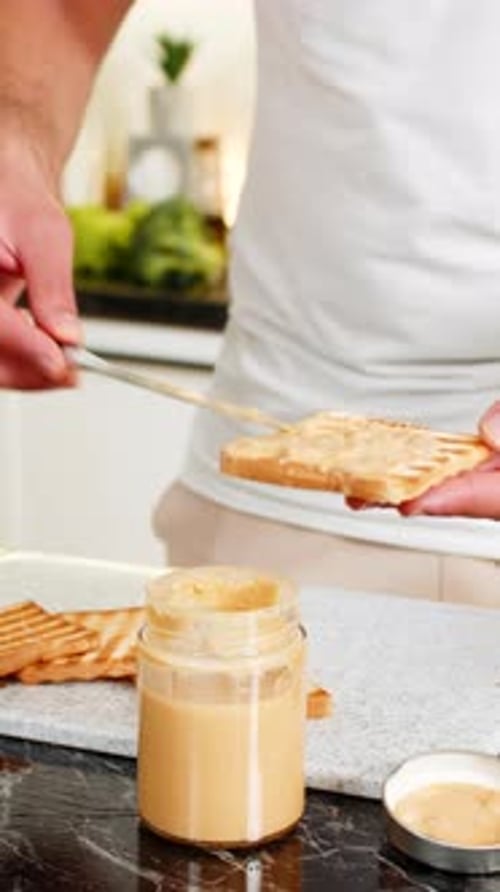 Préparer le petit-déjeuner en étalant du beurre de cacahuète sur une tranche de pain grillé à la maison, dans la cuisine, gros plan, chaud