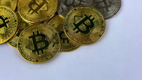 Silver and gold bitcoins slowly rotate on a white surface
