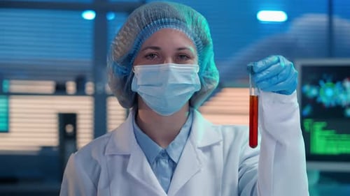 Una científica sostiene un tubo de ensayo con un líquido rojo en la mano y hace un gesto de parada con ella