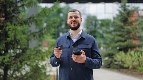 Hombre feliz con tarjeta de crédito y teléfono celebrando ganancias o ganancias al aire libre