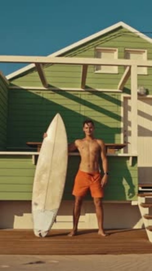 Surfer Posing with Surfboard at Beach Cabin