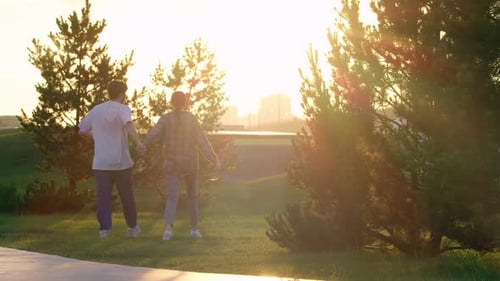 Young Couple Can Be Seen Walking in the Park During Sunset They are Holding Hands and Seem to Be