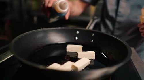 close-up chef puts tofu cheese on a hot pan fries it and pours sauces on it asian cuisine