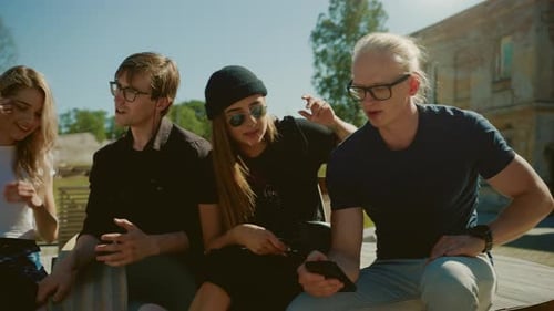 Stylish Cool Teenagers Chilling on the Benches in the Park, Using Smartphone. Two Girls and Two Boy