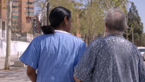 Rear View of a Caucasian Senior Woman Walking in the City with Her Internal Female Nurse Helper
