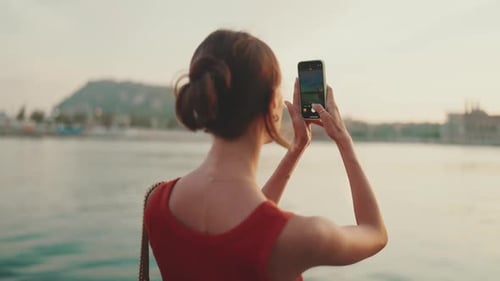 Close-up, girl stands on the embankment and takes pictures of sunrise on a mobile phone
